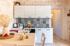 Una cocina moderna con armarios blancos, un salpicadero con diseño y una zona de comedor con una mesa dispuesta para dos.