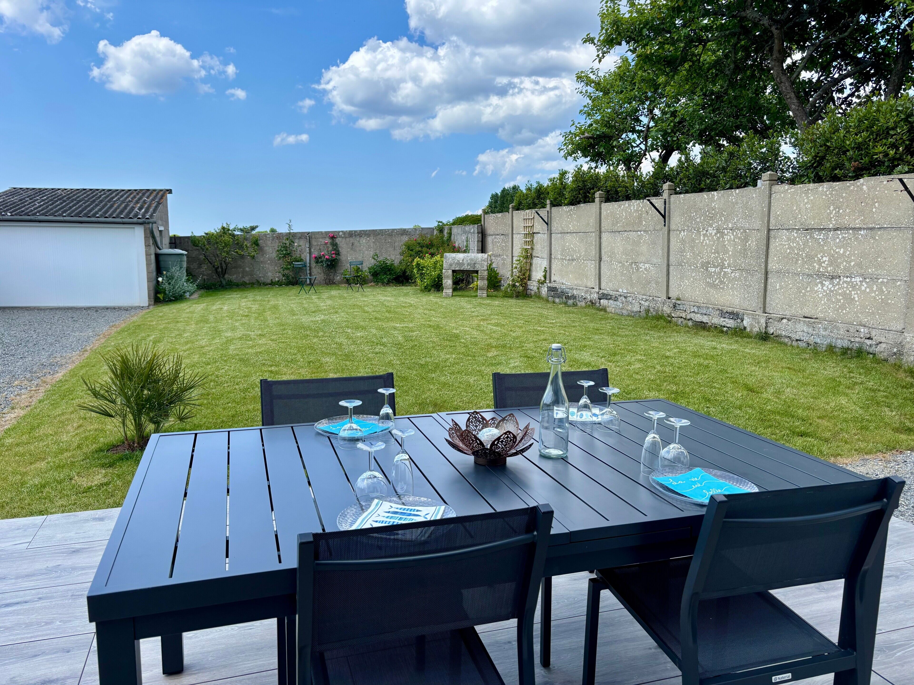 Eine Terrasse mit Esstisch, umgeben von Stühlen, einer kleinen Pflanze und einer Steinsäule.
