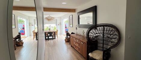 A spacious room with a wooden floor, a dining area with chairs, a large mirror, and a decorative chair.