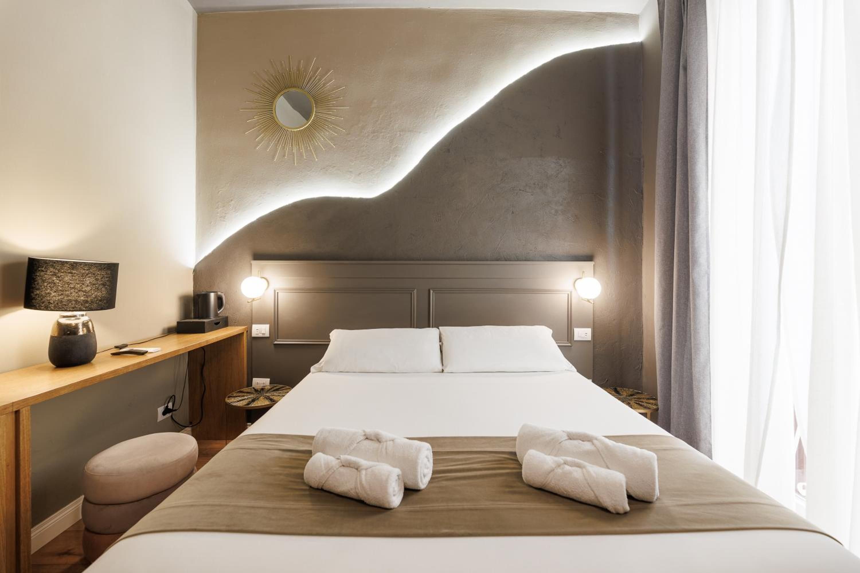 Ein Hotelzimmer mit einem Bett, Nachttischlampen, einem Nachttisch, einer Lampe, einem Wandspiegel und einem Fenster mit Vorhängen.