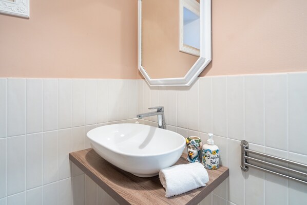 A bathroom with a white sink, a wooden vanity, a towel, a soap dispenser, and a towel rack.