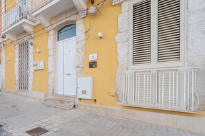Un edificio con fachada amarilla, puerta blanca y ventana con rejas.