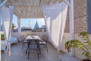 A covered outdoor seating area with a table and chairs, a view of a cityscape, and a potted plant.