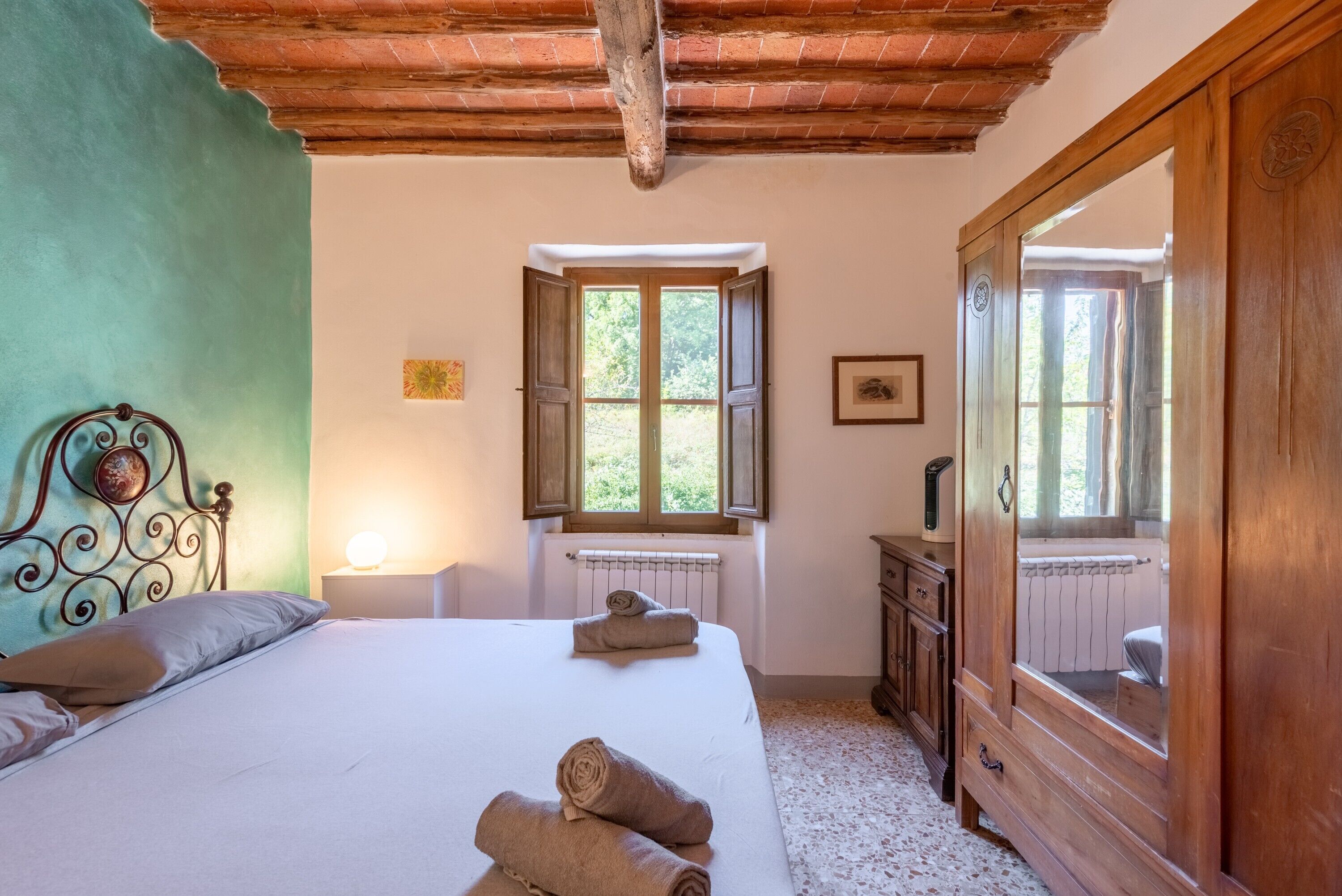 Une chambre à coucher avec un lit, une armoire en bois, une fenêtre avec des volets et un radiateur.