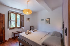 Een slaapkamer met een bed, een houten bankje, een raam en een hanglamp.