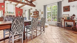 Comedor con mesa de madera y sillas a rayas de cebra, chimenea y vistas al exterior a través de ventanas amplias.