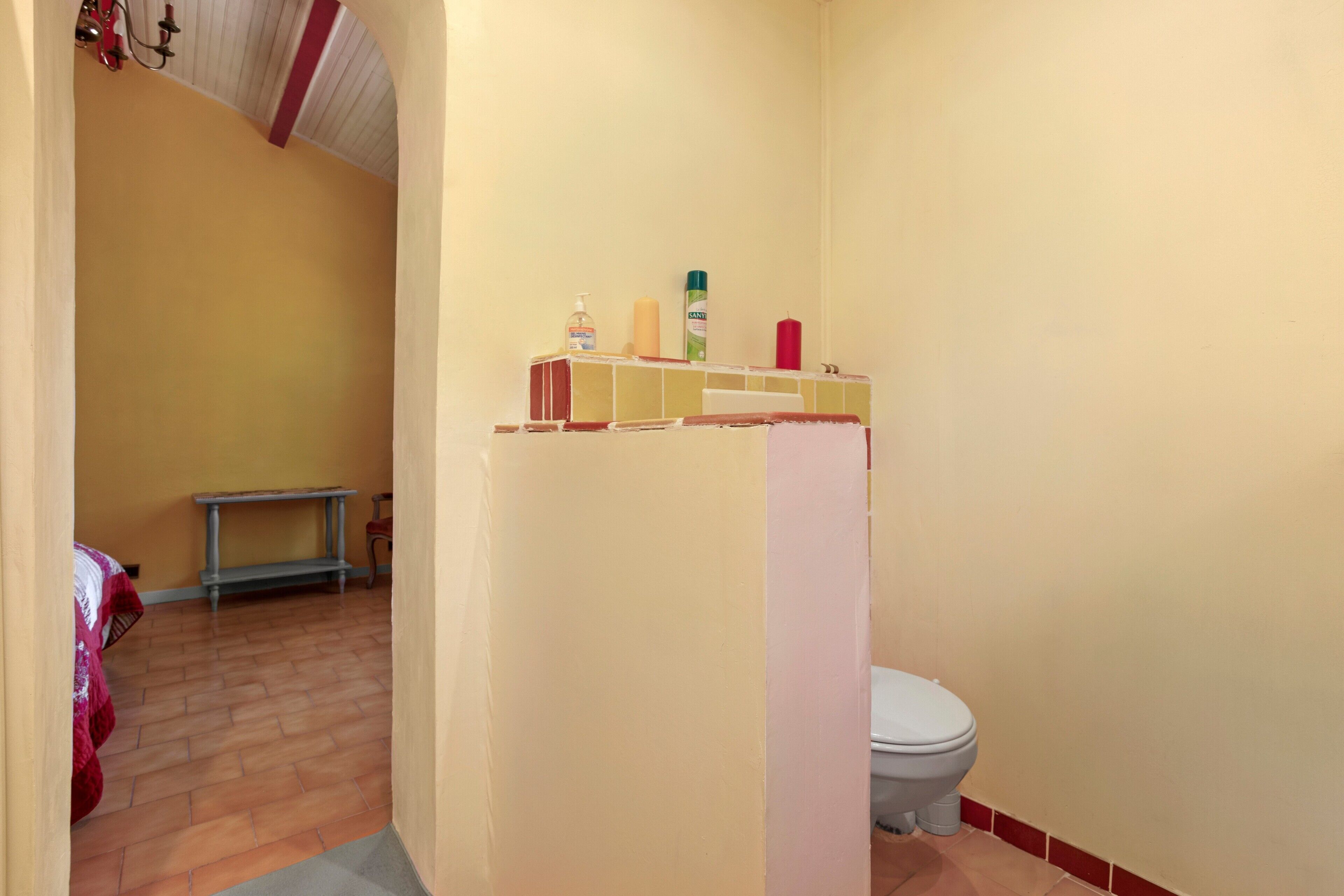 A bathroom with a toilet, a sink, and a mirror. There is a shelf with toiletries.
