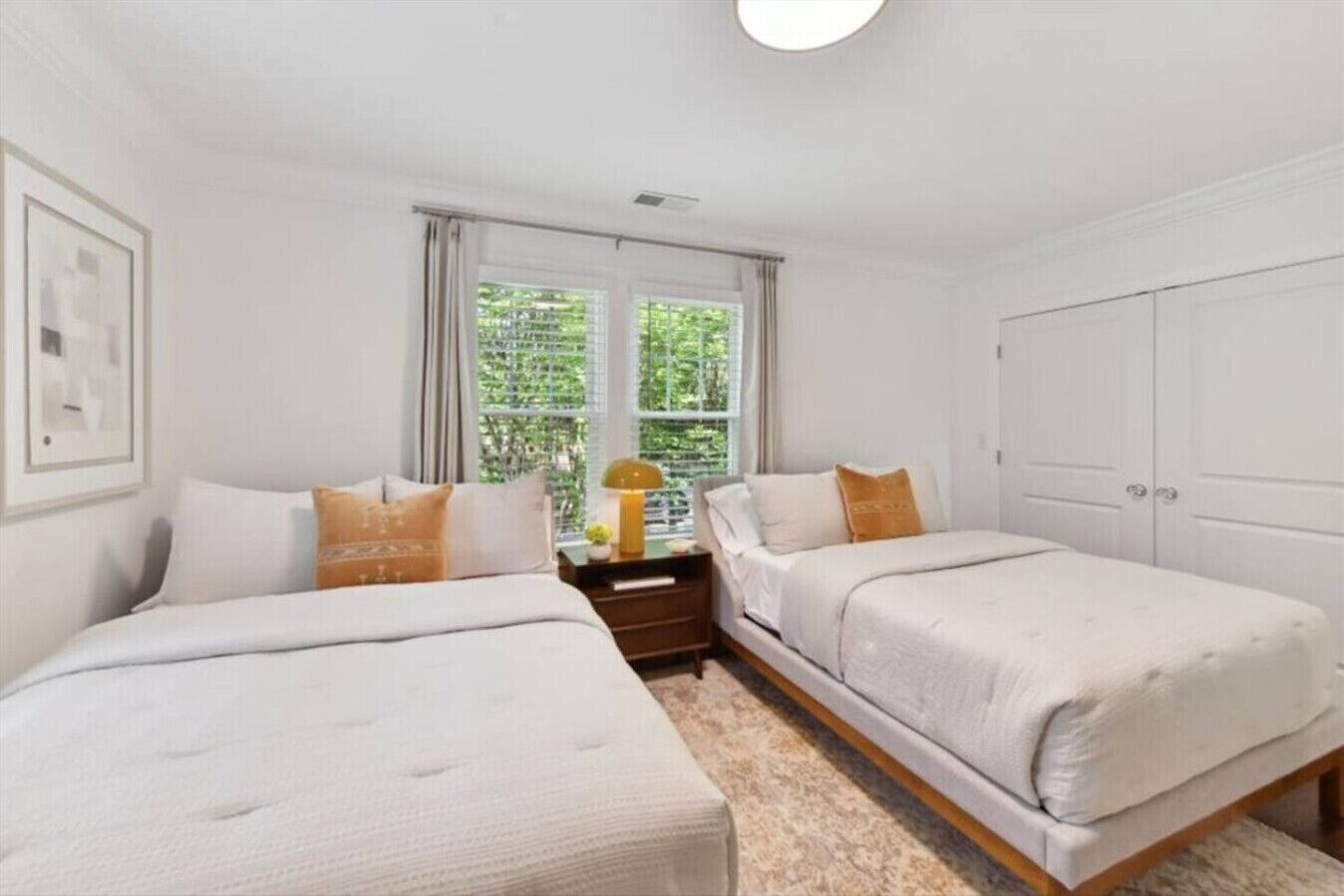 Quarto com duas camas de solteiro, mesa de cabeceira com abajur, janela com cortinas e guarda-roupa.