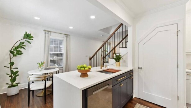 A modern kitchen with a white countertop, dark cabinets, and a wooden staircase.