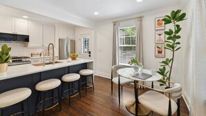 A modern kitchen with a central island, bar stools, and a dining area with a table and chairs.