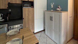 Een kleine keuken met houten kastjes, een magnetron en een eettafel met bestek.