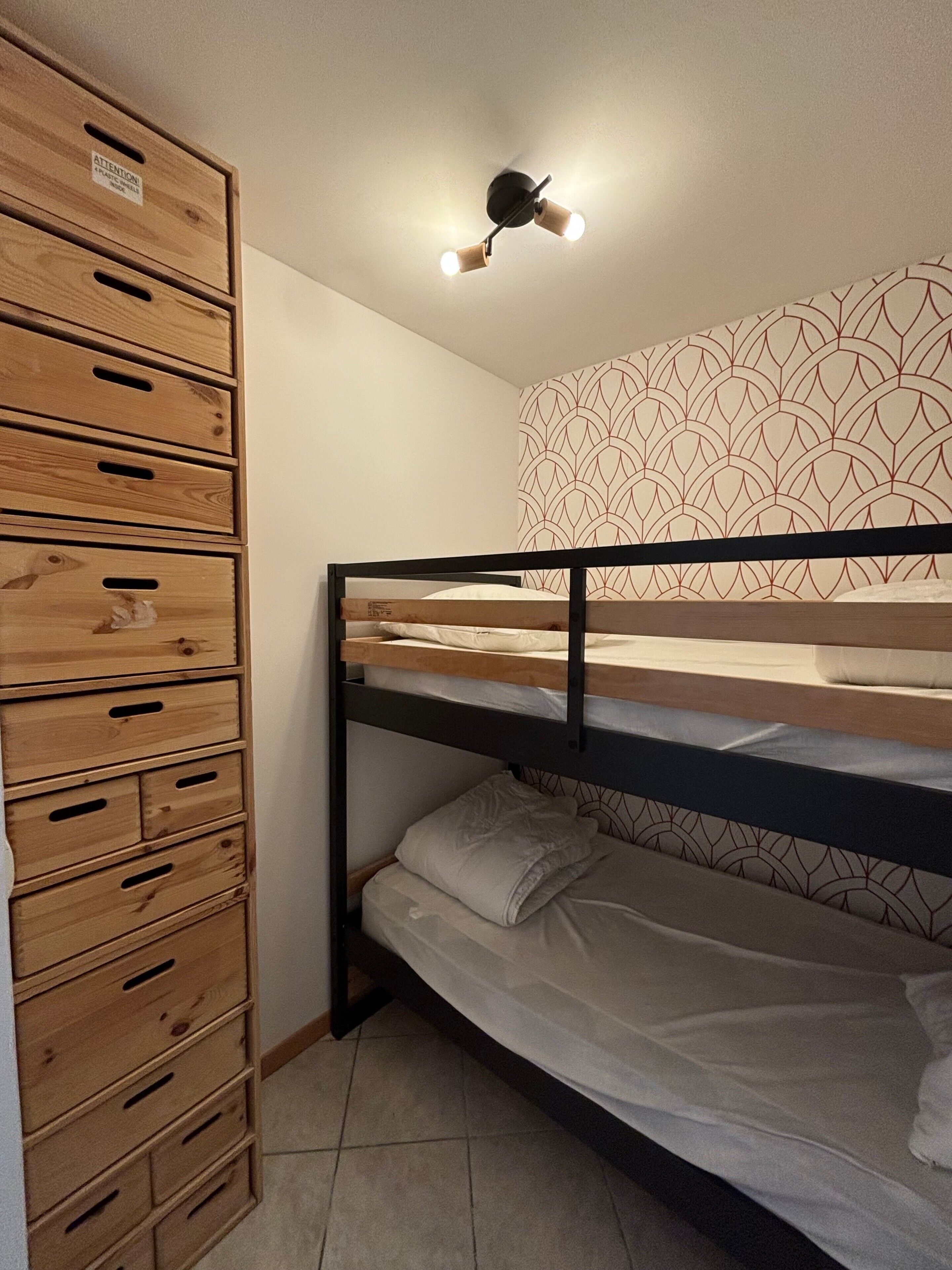 A bunk bed with a wooden headboard, a wall with a geometric pattern, and a ceiling light fixture.
