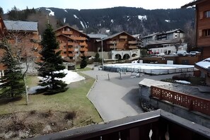 A mountainous village with wooden buildings, a paved courtyard, and a snow-covered mountain in the background.