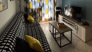 Een woonkamer met een bank, een salontafel, een televisie en een kamerbreed gordijn.