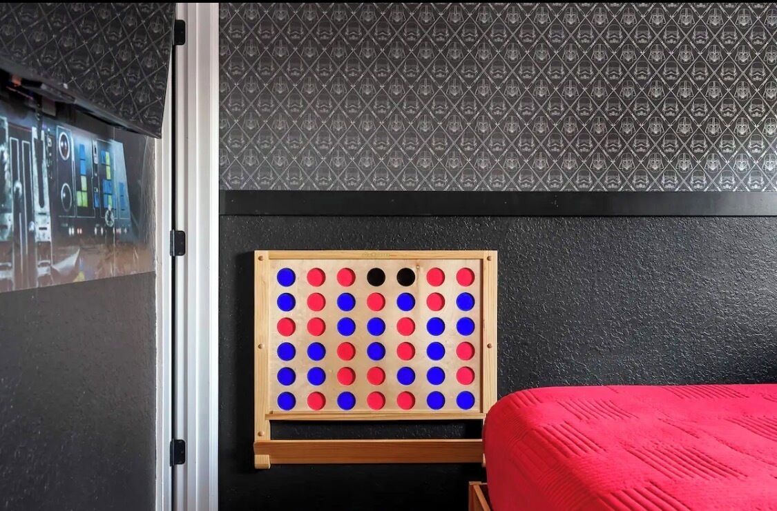 Ein Zimmer mit einem Nagelspiel, einem roten Bett und einer Wand mit Muster.