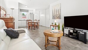 A modern living room with a white sofa, a wooden coffee table, a TV stand, and a dining area with chairs and a table. - Villa 'Les Coteaux Du Soleil' with Private Pool, Wi-Fi and Air Conditioning (Carcès)