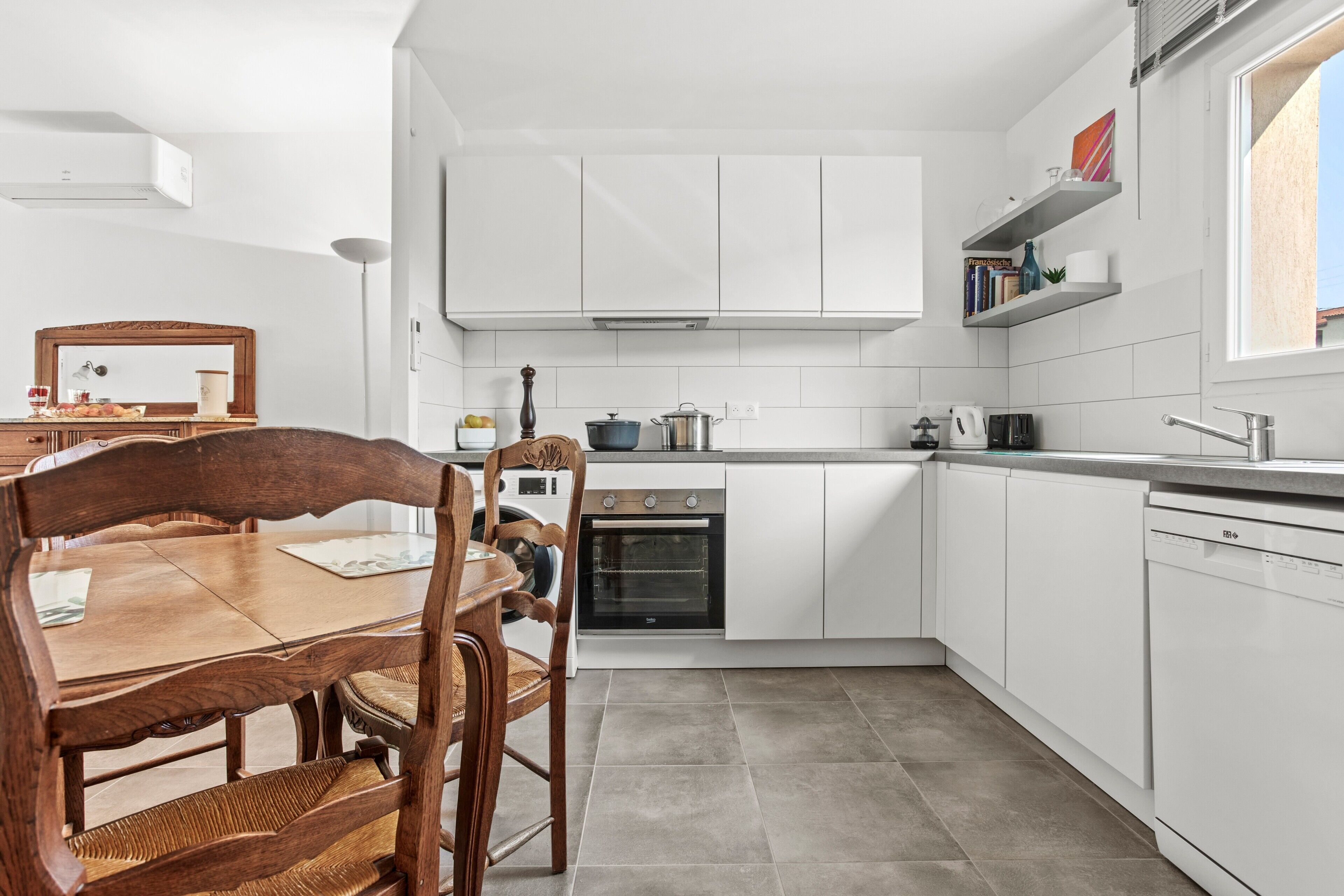 Eine moderne Küche mit weißen Schränken, einem Einbauofen und einem Essbereich mit einem Holztisch und Stühlen.