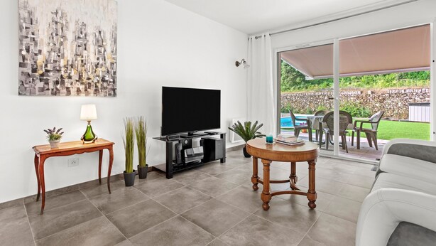 A living room with a flat-screen TV, a coffee table, a sofa, a painting, and a sliding glass door leading to an outdoor patio. - Villa 'Les Coteaux Du Soleil' with Private Pool, Wi-Fi and Air Conditioning (Carcès)