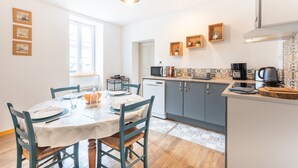 A modern kitchen with a dining area, featuring a white table, blue chairs, and a wooden floor. - Holiday Home 'Chez Bob' with Mountain View and Wi-Fi (Hèches)