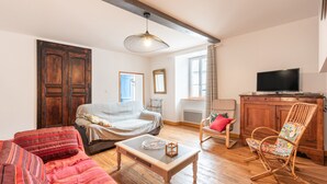 A living room with a sofa, a wooden coffee table, a wicker chair, a television, and a large wooden cabinet. - Holiday Home 'Chez Bob' with Mountain View and Wi-Fi (Hèches)