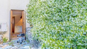 Un sendero de piedra que lleva a una puerta de madera, una parrilla en el exterior y una pared cubierta de flores blancas.