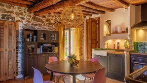 Una cocina rústica con paredes de piedra, vigas de madera y una mesa redonda con sillas.