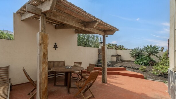An outdoor patio with a wooden table and chairs, a pergola, and a view of a garden. - Holiday Home 'Aguarijo' with Sea View, Private Terrace and Private Garden (El Mocanal)