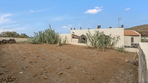 A single-story building with a flat roof, surrounded by a dirt yard with sparse vegetation. - Holiday Home 'Aguarijo' with Sea View, Private Terrace and Private Garden (El Mocanal)