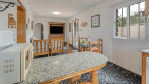 A kitchen with a granite countertop, wooden chairs, a microwave, and a television. - Holiday Home 'Aguarijo' with Sea View, Private Terrace and Private Garden (El Mocanal)