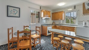 A kitchen with wooden cabinets, a granite countertop, a dining table with chairs, and a bar stool area. - Holiday Home 'Aguarijo' with Sea View, Private Terrace and Private Garden (El Mocanal)