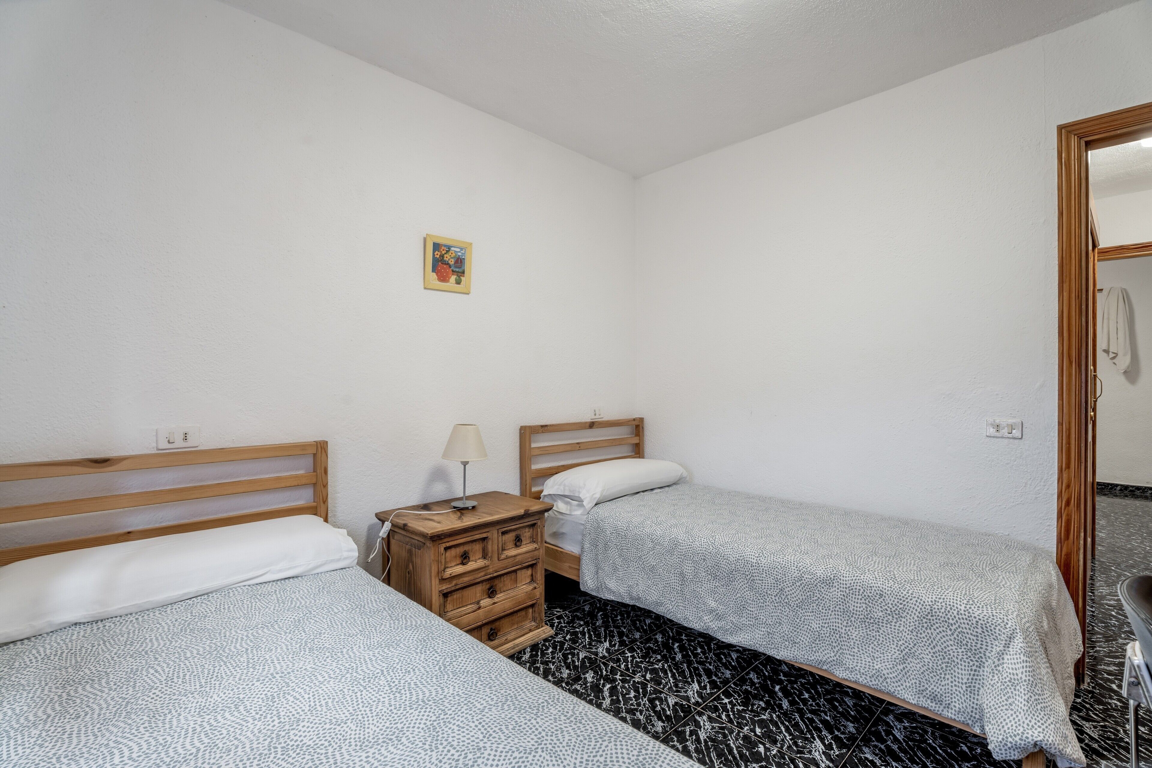 Un dormitorio con dos camas, un aparador de madera, un cuadro pequeño en la pared y un espejo.