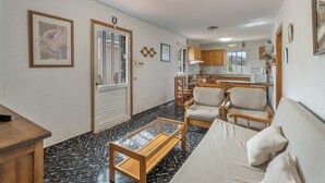 A living room with a sofa, chairs, a coffee table, a wooden desk, and a door leading to a kitchen. - Holiday Home 'Aguarijo' with Sea View, Private Terrace and Private Garden (El Mocanal)