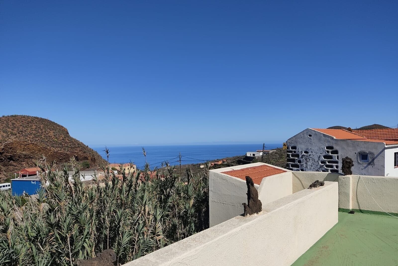 Vista costera con edificios, cielo despejado y una montaña distante.
