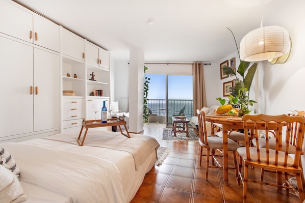 Un dormitorio con cama, mesita de noche de madera, escritorio y silla, y balcón con vistas.