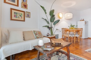 Una sala de estar con sofá, mesa de centro, mesa de comedor, sillas y una obra de arte en la pared.