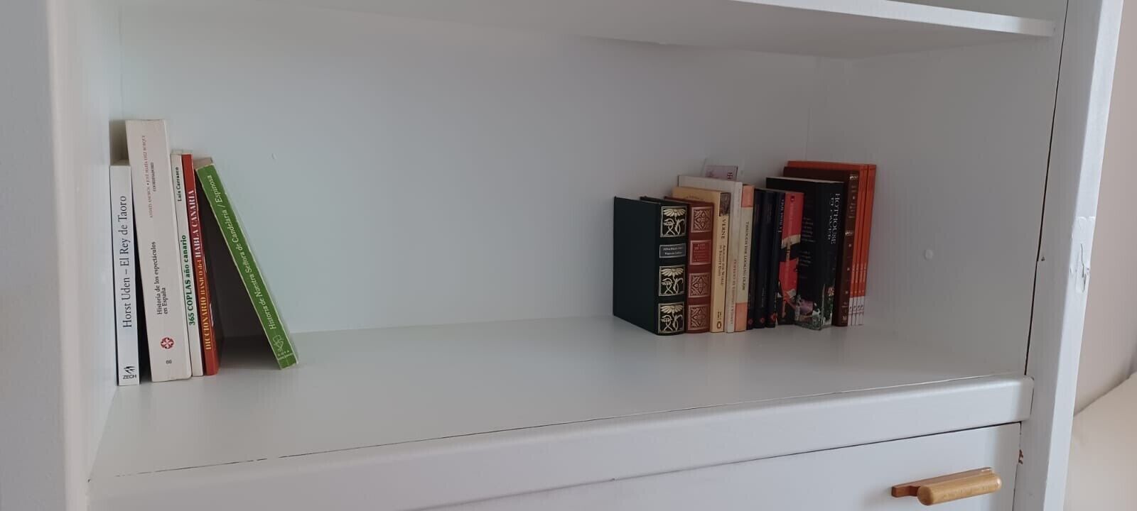 A white bookshelf with books, a wooden handle drawer, and a white wall.