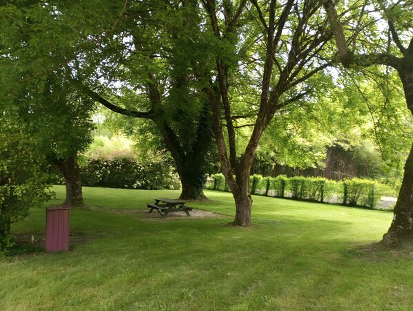 A park with a picnic table and benches, surrounded by trees and a well-maintained lawn.