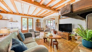Un salón acogedor con techo de madera, chimenea de piedra, televisor y comedor.