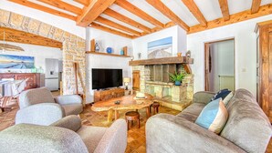Amplia sala de estar con chimenea de piedra, vigas de madera y televisor.