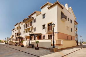 A multi-story residential building with balconies, a tiled courtyard, and street lamps. - Golf Relax In Betanzos Apartment with Shared Pool, Wi-Fi, and Air Conditioning (Fuente Alamo)