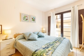 A bedroom with a bed, nightstands, wall art, and a view through a window.