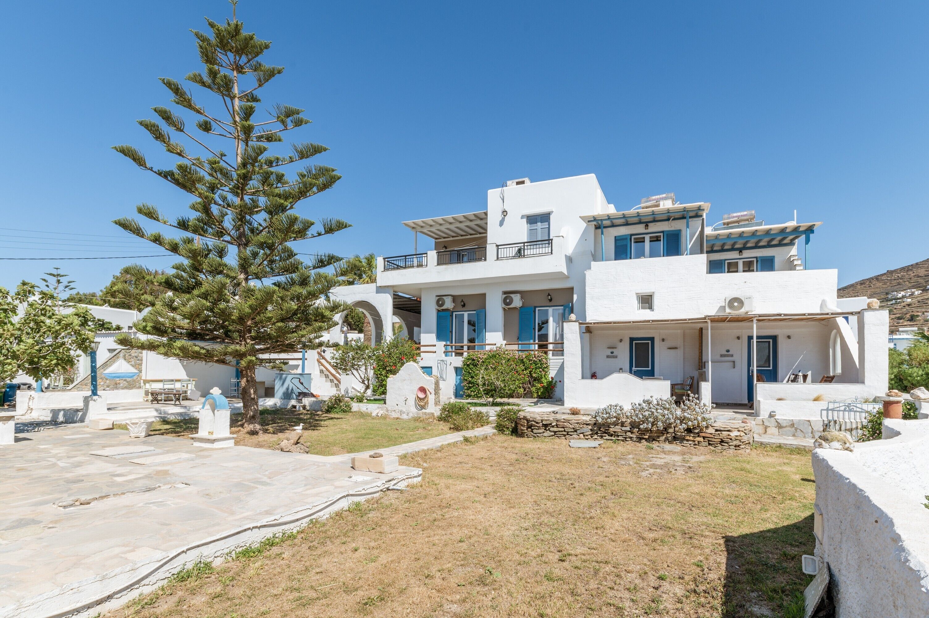 A white building with blue accents, a stone pathway, and a pine tree.