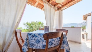 Un espacio de comedor al aire libre techado, con una mesa y sillas, y vistas a follaje y montañas, con techo de madera.