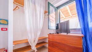 Un dormitorio con un aparador de madera, un televisor encima, una ventana con vistas y una cama con dosel blanco.