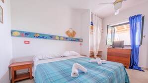Un dormitorio con cama, una mesita de noche de madera, un escritorio con un ordenador portátil, una ventana con cortinas y adornos en la pared.
