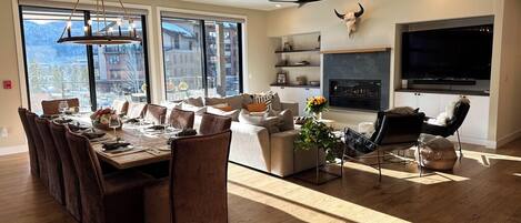 A spacious living room with a fireplace, a dining area with a long table, and a large window offering a mountain view.