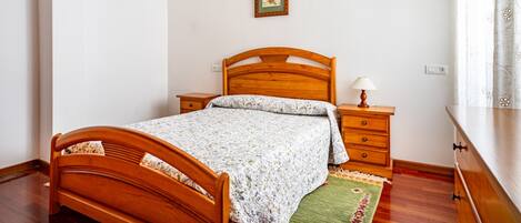 A bedroom with a wooden bed, a nightstand, a dresser, a framed picture on the wall, and a window with curtains.