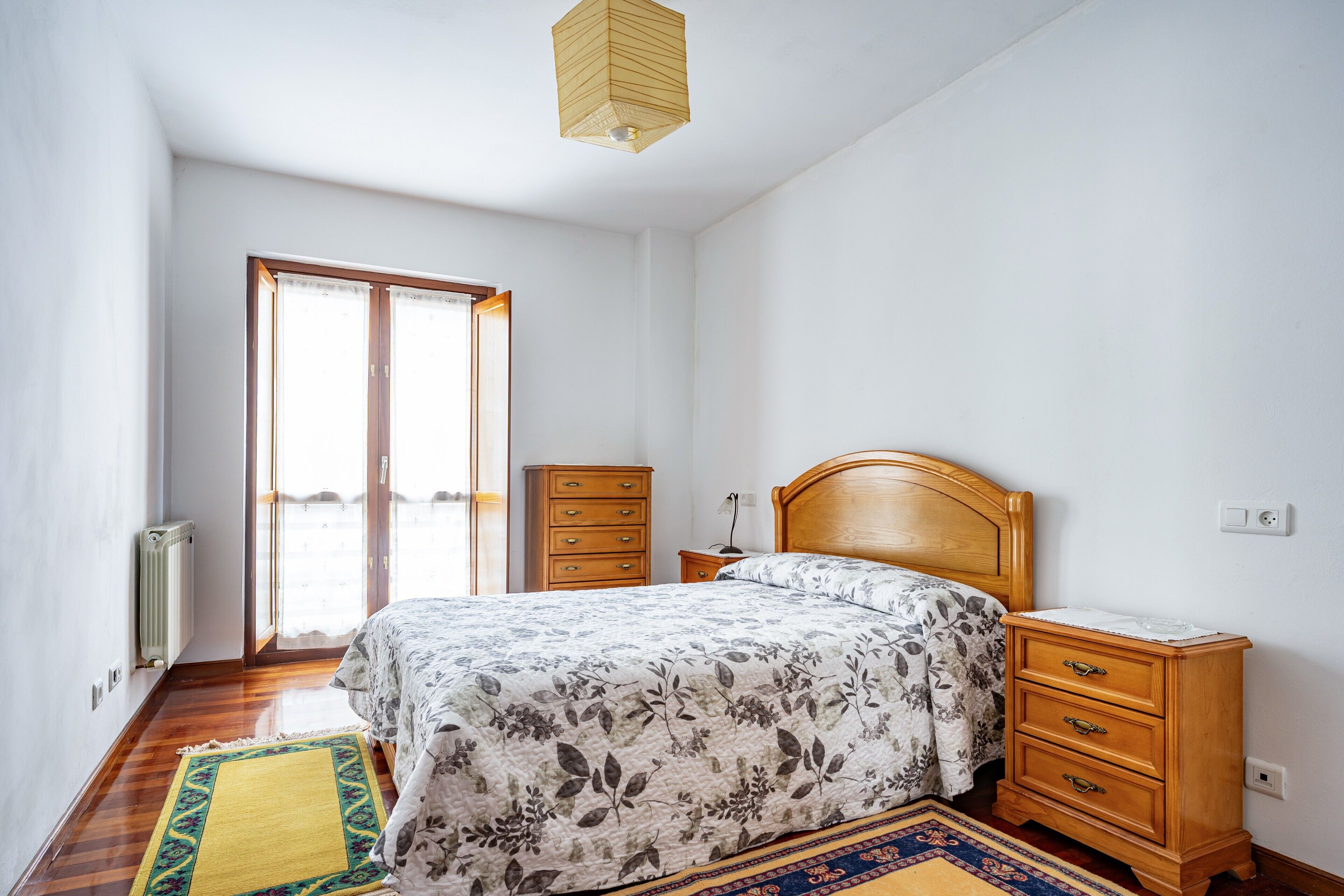 Un dormitorio con cama, cómoda de madera y un radiador.