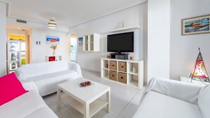 A modern living room with white furniture, a flat-screen TV, and decorative items. - 'Incredible Playazo Vera' Apartment with Shared Pool, Private Terrace & Air Conditioning (Vera)
