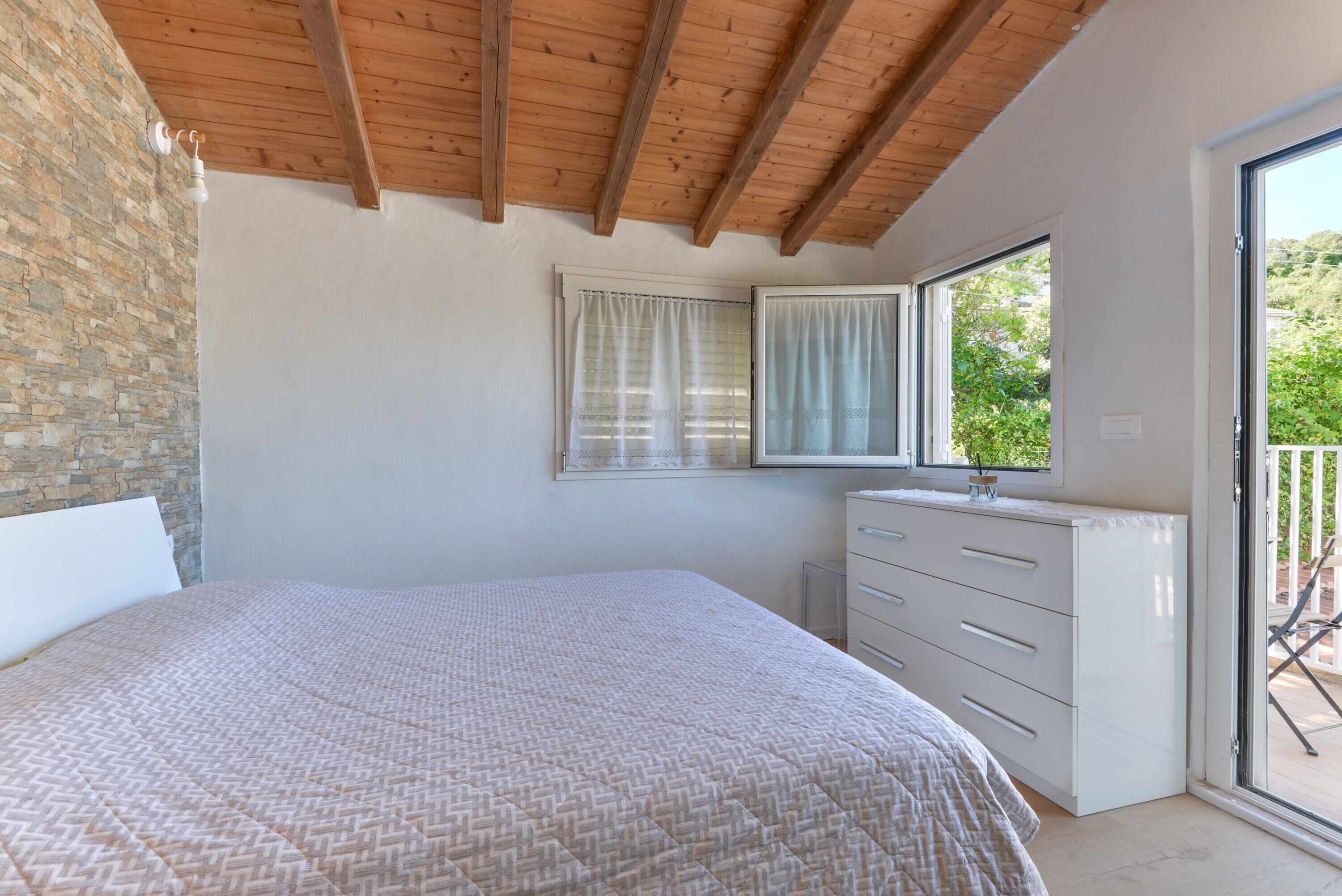 Une chambre à coucher avec un lit, une commode, une fenêtre avec des rideaux et un balcon.